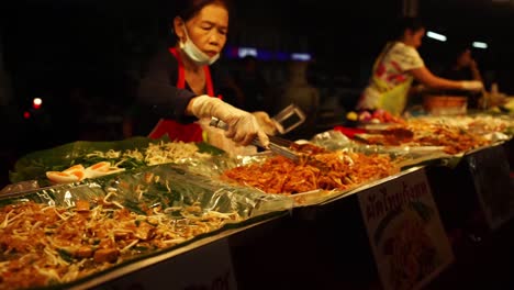 Comida-Callejera-Asiática---La-Vendedora-Tailandesa-Detrás-Del-Mostrador-Pone-Comida-Al-Comprador