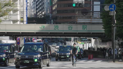 Strom-Von-Taxis-Und-überfressenden-Radfahrern,-Die-Während-Der-Pandemie-Ohne-Touristen-In-Tokio,-Japan,-An-Der-Shibuya-kreuzung-Vorbeifahren