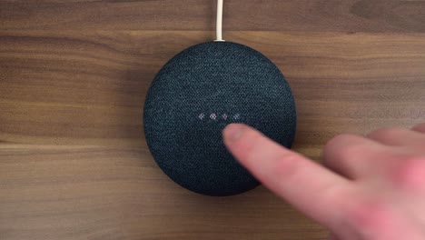 Finger-pressing-on-a-Google-Nest-Home-Mini-smart-speaker-with-built-in-Google-Assistant