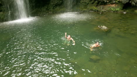 Dos-Excursionistas-Masculinos-Nadan-Y-Se-Relajan-En-La-Piscina-Junto-A-Las-Cataratas-Waikani-En-El-Camino-A-Hana,-Maui