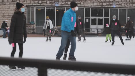 Handheld-shot-of-people-ice-skating-at-public-rink-wearing-Covid-19-masks