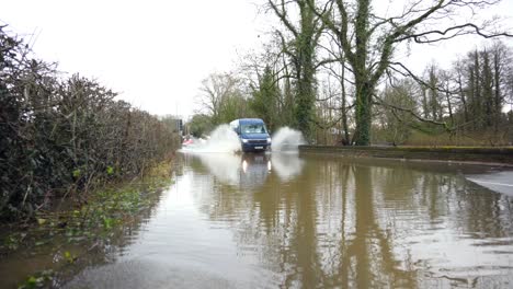 Flooded-road-with-van-driving-through,-showing-the-river-Bollin-and-river-Dean-in-Wilmslow,-Cheshire-after-heavy-rain-and-with-burst-banks