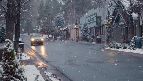 Solo-car-driving-up-empty-Christmas-street-snowfall-welcome-sign,-tracking-shot