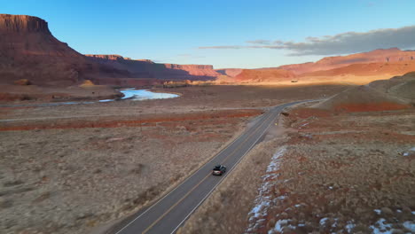 A-drone-follows-a-car-along-an-empty-road-along-the-Colorado-River-near-Moab,-Utah