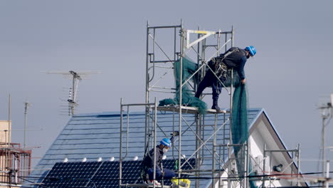 Japanese-Construction-Workers-Working-And-Putting-Safety-Net-On-Scaffoldings-During-Pandemic-In-Tokyo,-Japan