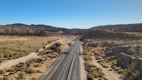 Vehicles-drive-along-a-dirt-road-beside-empty-train-tracks-in-Afton-Canyon,-in-the-Mojave-Desert-of-California