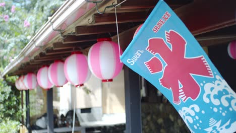 Flagge-Weht-Im-Wind-Mit-Laternen,-Die-An-Der-Seite-Der-Dächer-Eines-Restaurants-In-Kyoto,-Japan,-Zeitlupe-4k-Hängen