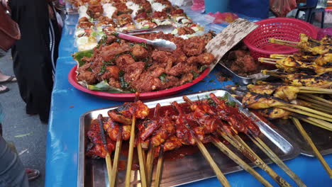 Colourful-and-multiple-type-of-meat-bbq-on-skewers-put-on-display-with-people-buying-it