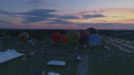 Luftaufnahme-Von-Heißluftballons,-Die-Sich-Für-Eine-Nächtliche-Flammenshow-Bei-Einem-Ballonfestival-Bei-Sonnenuntergang-Füllen,-Wie-Von-Einer-Drohne-Gesehen