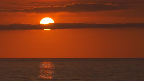 Big-orange-sun-with-clouds-over-ocean-at-sunrise,-mediterranean-dawn