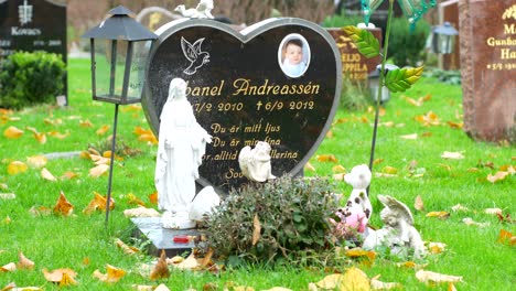 A-young-boy's-tombstone-with-the-Catholic-statues-in-Kviberg-Cemetery-in-Gothenburg,-Sweden---panning-shot