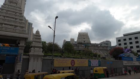 People-Walking-On-The-Side-Walk-Going-To-Temple-In-ISKON-Bengaluru,-India-With-A-Calm-Weather-Seeing-The-Cloudy-Sky---Wide-Shot