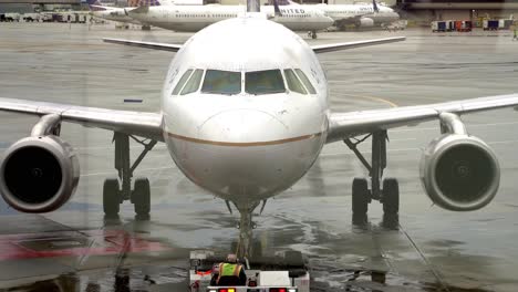 Close-up-front-view-of-a-Boeing-jet-being-pushed-back-from-a-gate-at-San-Francisco-airport-on-a-rainy-afternoon