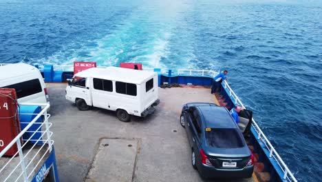 Top-view-deck-of-a-large-ship-carrying-cars-with-people-watching-over-the-ocean-while-the-ship-is-on-the-run-over-a-blue-ocean