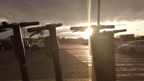 Sonneneruption-Hinter-Vermietung-E-Scooter-Bei-Sonnenuntergang-Mit-Autos-Im-Hintergrund