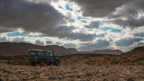 Time-lapse-of-cloudscape-over-4WD-vehicle-parked-in-desert,-zoom-in