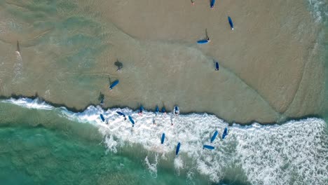 Aerial-drone-shot-looking-down-on-a-large-group-of-people-learning-to-surf-at-the-beach