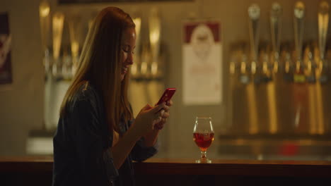 Mujer-Soltera-Feliz-En-El-Bar-Enviando-Mensajes-De-Texto-Por-Teléfono-Celular,-Tiro-Medio-En-La-Noche