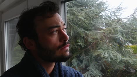 Close-up-of-young-male-wakes-up-early-morning-and-looks-out-bedroom-window-looking-thoughtful-pensive-worried