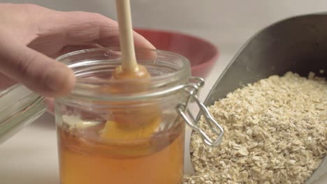 Hand-stirring-pot-of-golden-runny-honey-with-scoop-of-oats