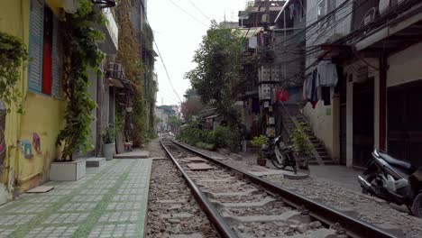 Man-crosses-tracks-at-Train-Street-showing-buildings-close-to-the-tracks-with-mopeds-parked,-Locked-shot
