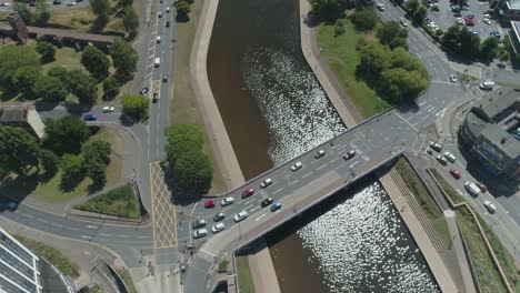 Top-down-of-a-busy-multi-lane-traffic-junction-or-lights-controlled-roundabout-over-a-shimmering-river