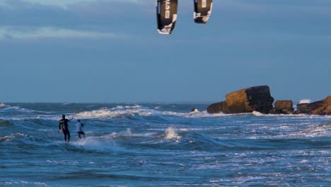 A-group-of-people-engaged-in-kitesurfing-in-sunny-autumn-day,-high-waves,-Baltic-Sea-Karosta-beach-in-Liepaja