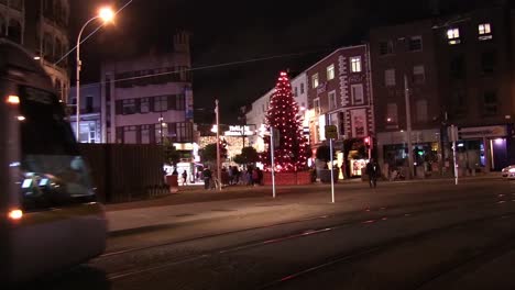 Still-shot-of-the-Luas-tram-passing-by-and-Christmas-tree-on-Graton-St-with-people-flocking-around-it