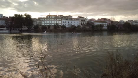 Menschen-In-Der-Ferne-Rudern-Kanus-Auf-Dem-Fluss-Guadalquivir-In-Der-Abenddämmerung,-Sevilla,-Spanien