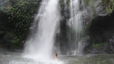 Woman-standing-in-strong-waterfall,-powerful-in-the-jungle