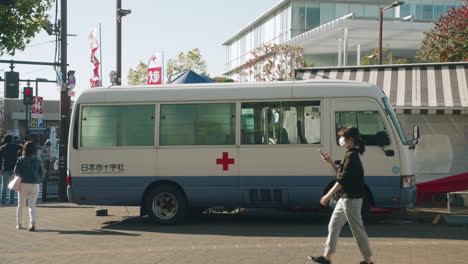 People-In-Face-Mask-Passing-By-Bloodmobile-Parked-On-The-Red-Cross-Blood-Donation-Station-In-The-Street-Of-Tokyo-During-The-COVID-19-Outbreak-In-Tokyo,-Japan