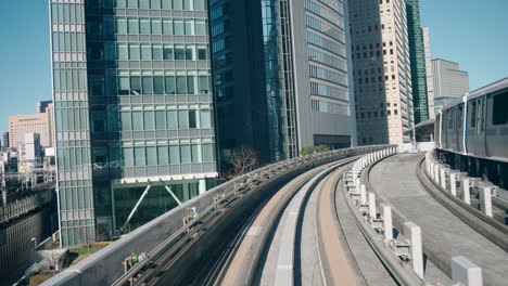 A-point-of-view-shot-of-a-Yurikamome-monorail-arriving-at-a-station-with-skyscrapers-in-the-background-in-Tokyo,-Japan