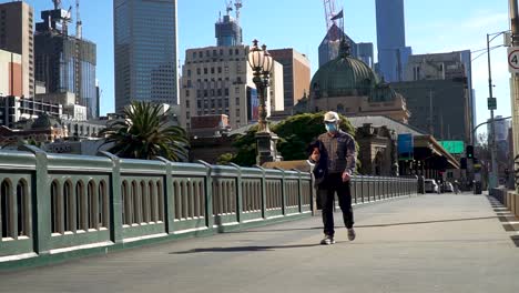 Man-wearing-a-mask-crosses-Melbourne's-famous-city-bridge-during-strict-coronavirus-lockdown-restrictions---Victoria,-Australia