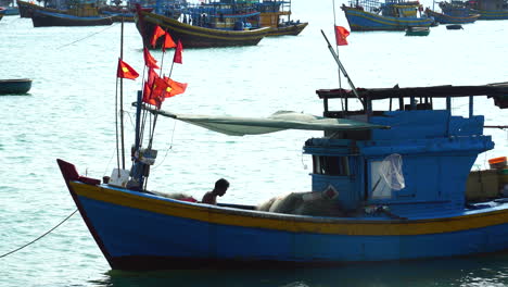 Silhouette-of-fisherman-on-boat-fixing-net,-flags-of-Vietnam-in-wind