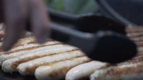 Close-up-of-Grill-master-flipping-sausages-for-guests-on-gas-bbq-at-dinner-party