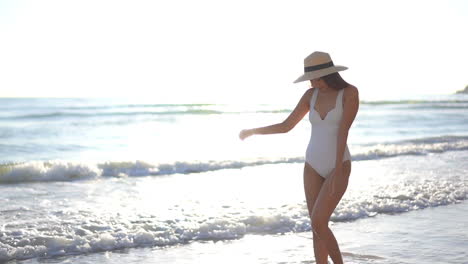 Sexy-Woman-in-White-Swimsuit-and-Summer-Hat-Walking-on-Sandy-Beach-by-Tropical-Sea-Waves,-Slow-Motion