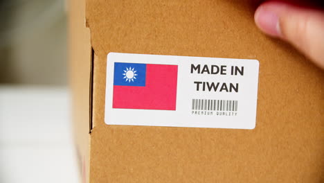 Hands-applying-MADE-IN-TIWAN-flag-label-on-a-shipping-cardboard-box-with-products