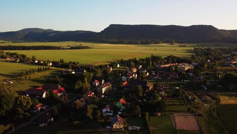 Czech-village-Martinkovice-and-Broumov-Walls,-forested-mountain-ridge,-behind-it