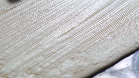 Extreme-close-up-on-softened-butter-being-brushed-on-freshly-rolled-shoot-of-flat-dough