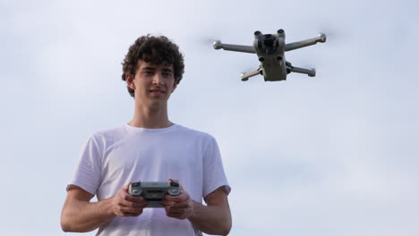 Young-Drone-Pilot-Controlling-DJI-Mavic-Mini-3-Pro-Quadcopter-Aircraft-With-Controller,-Flying-Up-in-The-Air,-Slow-Motion