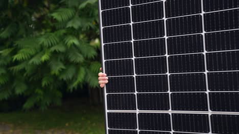 Person-carrying-large-black-Solar-Panel-on-backyard,-only-hands-visible
