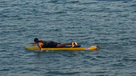 Young-boy-rowing-with-hands-while-lying-on-a-yellow-board,-slow-motion