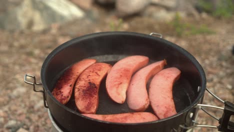 Pan-right-across-hot-fry-pan-cooking-sausages-on-camp-stove-outdoors