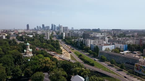 Warsaw,-Poland,-Aerial-View-of-Orthodox-and-Catholic-Church-in-Suburbs-With-Downtown-in-Skyline,-Drone-Shot