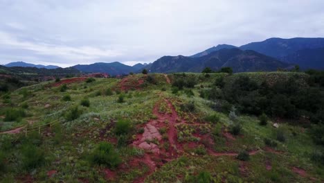 Rising-shot-of-red-rock,-green-grass,-and-mountains-in-Colorado