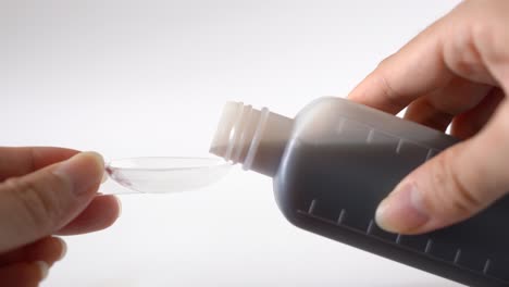 Close-up-female-hands-pouring-medicine-syrup-to-measuring-spoon-from-bottle-for-flu-treatments