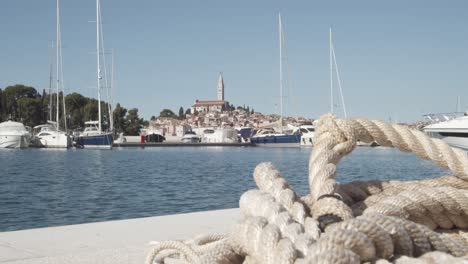 Close-up-shot-of-ship-rope-lying-on-ground-with-luxury-boats-and-Rovinj-Island-in-background