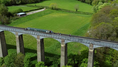 Aerial-view-following-narrow-boat-on-Trevor-basin-Pontcysyllte-aqueduct-crossing-in-Welsh-valley-countryside-zoom-out-reveal