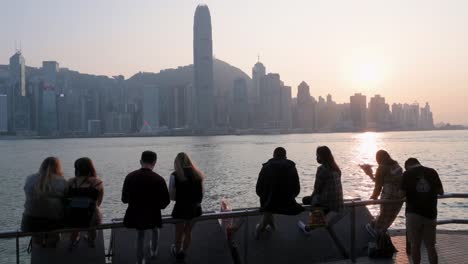 Menschen-Versammeln-Sich-Entlang-Der-Uferpromenade-Von-Victoria-Harbour,-Während-Sie-Den-Blick-Auf-Die-Skyline-Von-Hongkong-Genießen,-Während-Der-Sonnenuntergang-Einsetzt