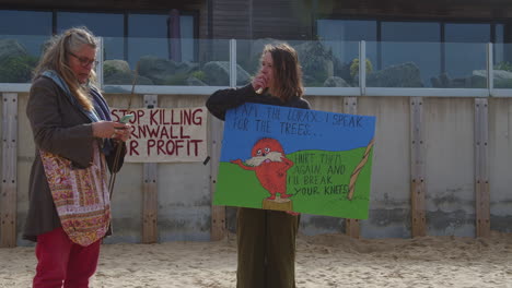 Two-female-protesters-talking-and-laughing-whilst-standing-on-beach-in-front-of-Carbis-Bay-Hotel-in-St